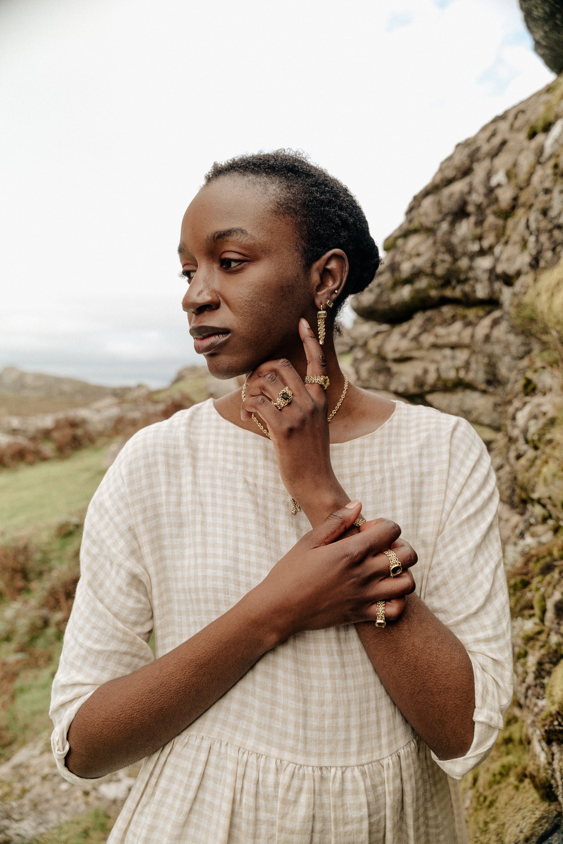 A model wearing lots of gold chain mail rings, earrings necklace and bracelet. Gold chains draping with sapphire gemstones.