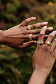 wide yellow gold chainmail bands dress the fingers of a model. Each ring has a large sapphire of mixed green, blue, yellow hues. 