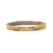 A yellow and white gold chain link bracelet made of handmade links woven with geometric patterns to create a chainmail bangle. on a white background.