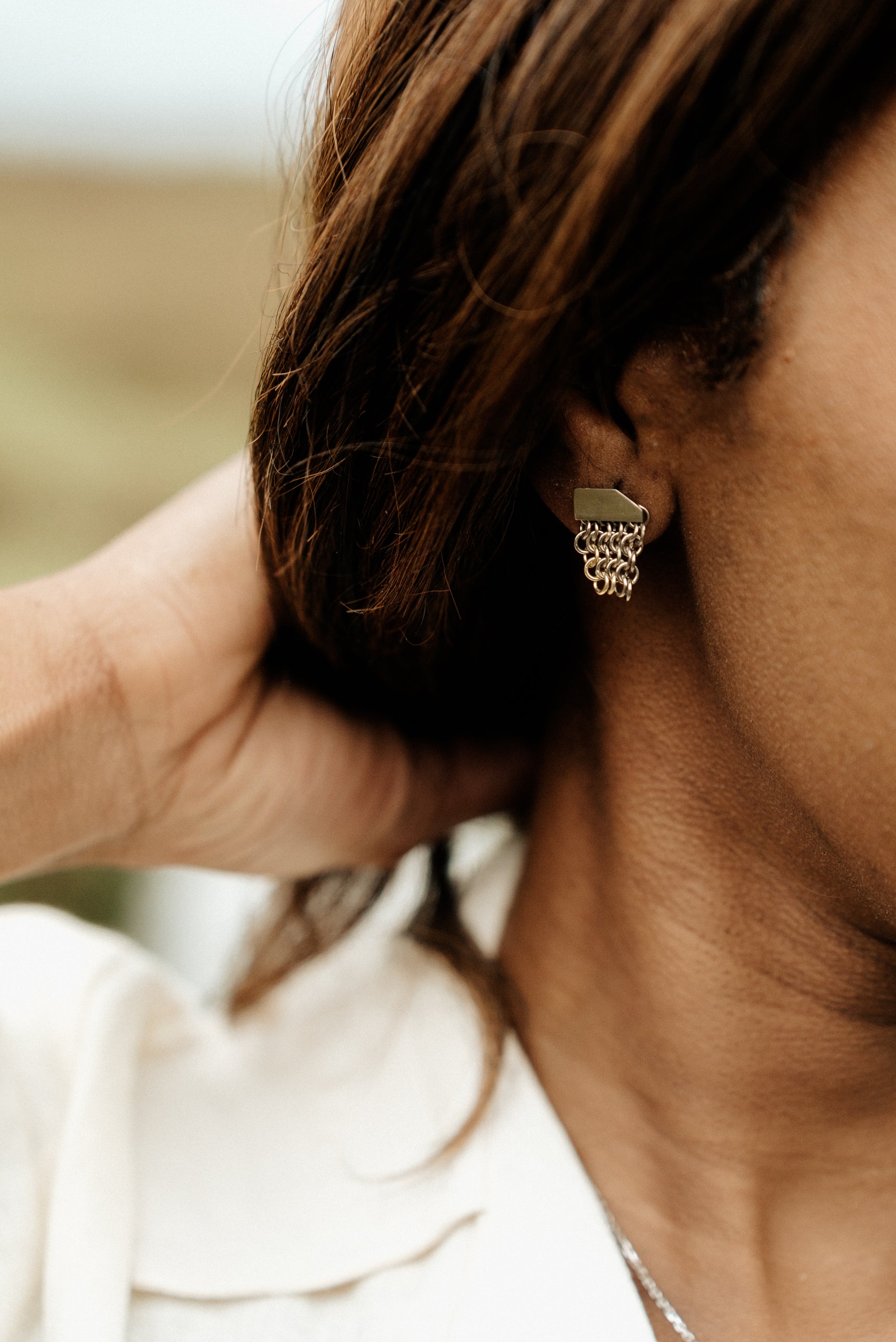 A single image of 18ct white gold stud earrings with a yellow gold edging on one corner, featuring a flat bar at the lobe with a short section of chainmail chain dangling down.