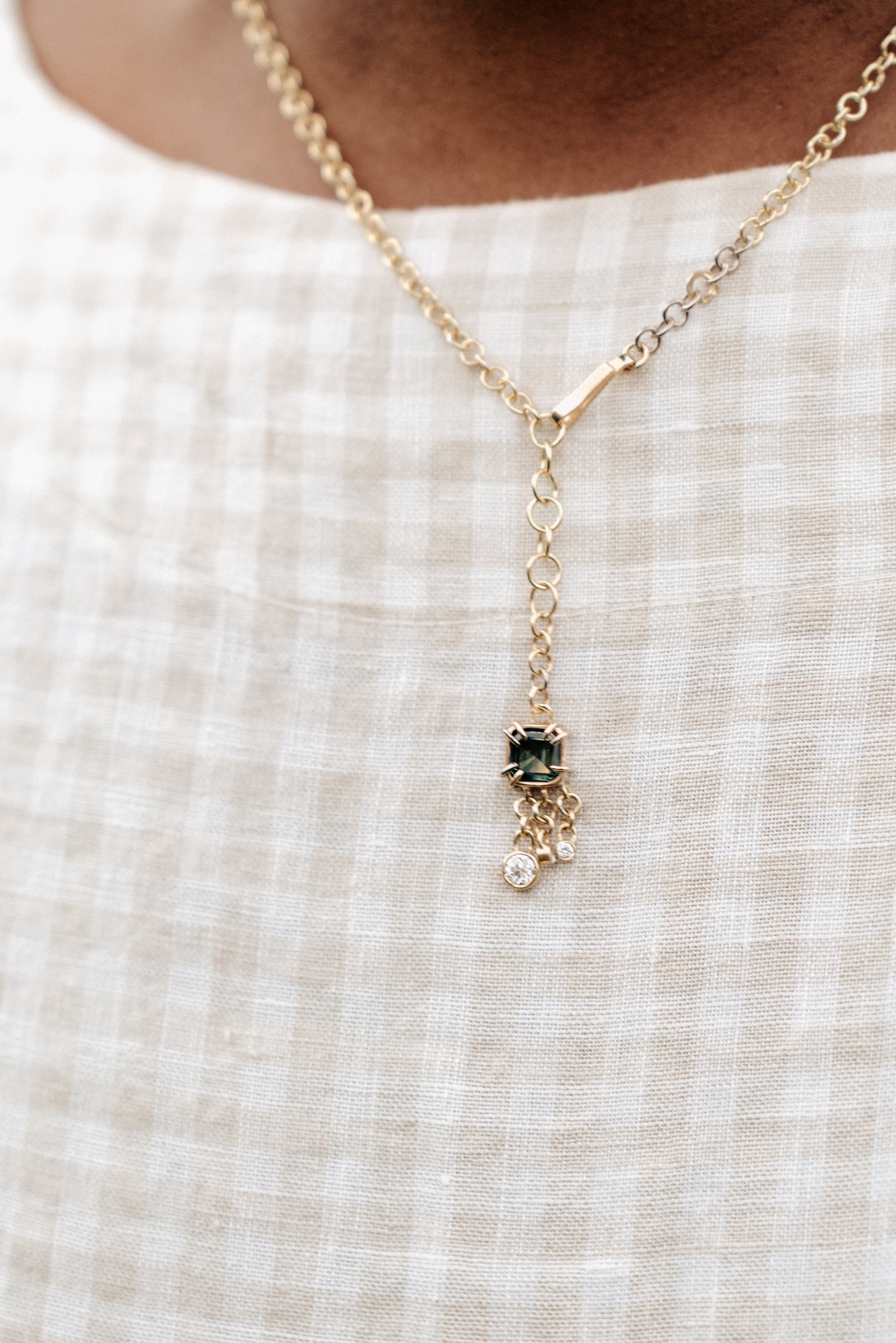 A solid gold necklace with a square-cut Australian Parti Sapphire pendant and three dangling diamonds, worn on a checkered white background.