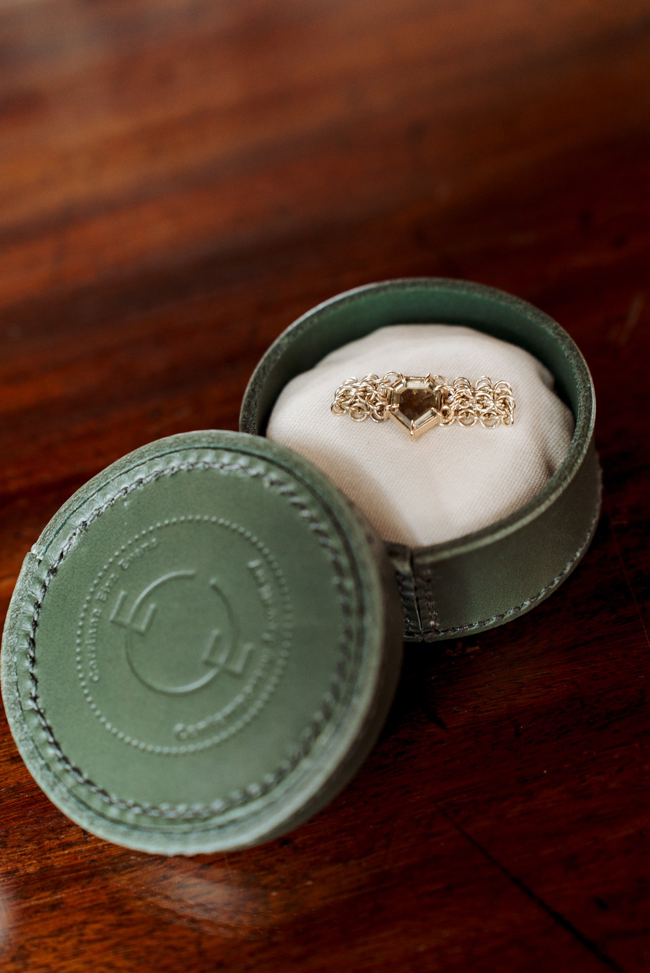 gold yellow chainmail ring with angular light green sapphire ring in green leather hand stitched ring presentation box