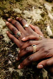modelled hands overlapping with close up image of four yellow gold chain link bands. Each chainmail ring has a green, blue, yellow parti sapphire in different shapes as their centrepiece. Two have claw settings and two have smooth rub over settings.