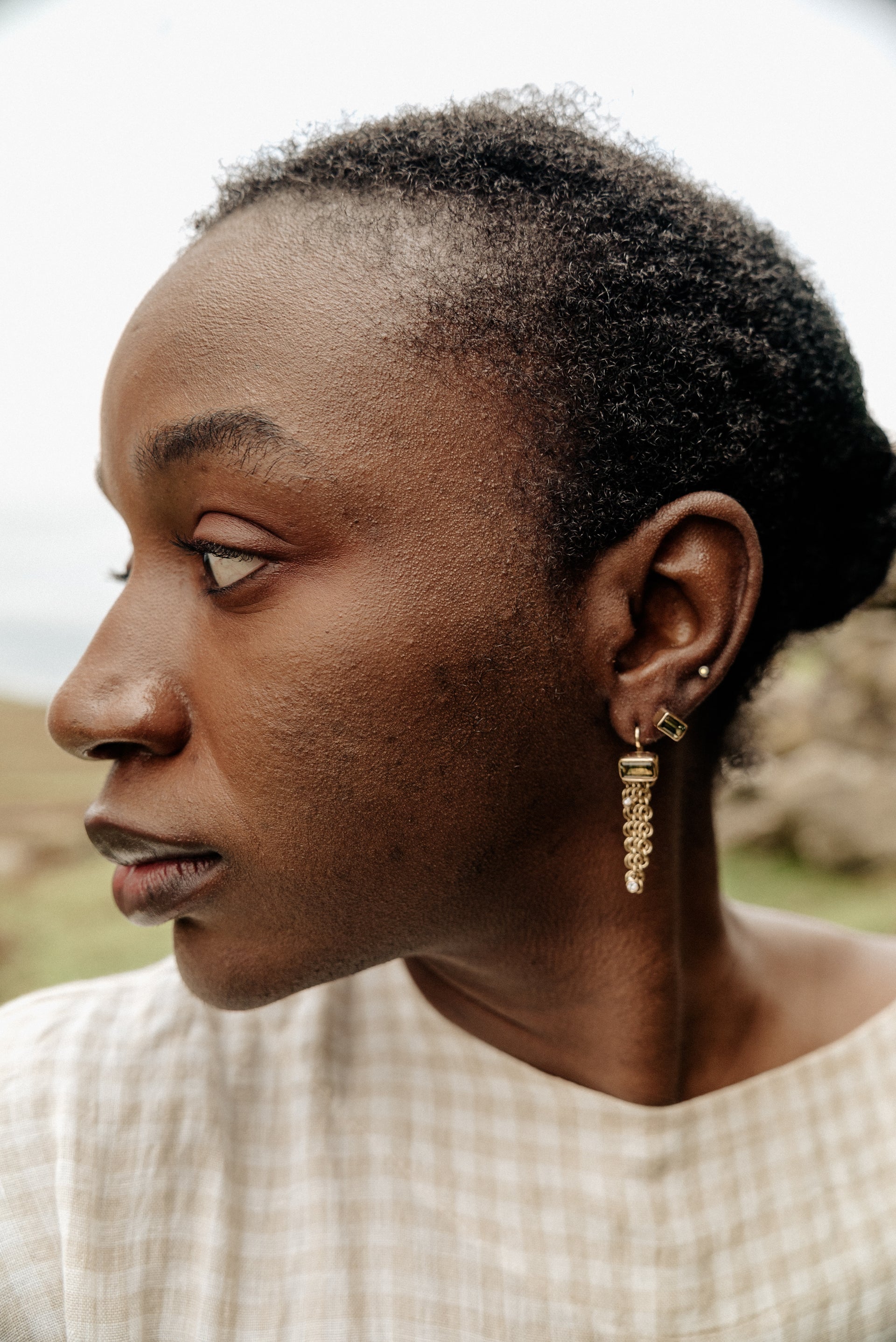 yellow gold hook earring with a green sapphire centre gemstone at the top and a length of dangling chainmail with two white diamonds on each earring